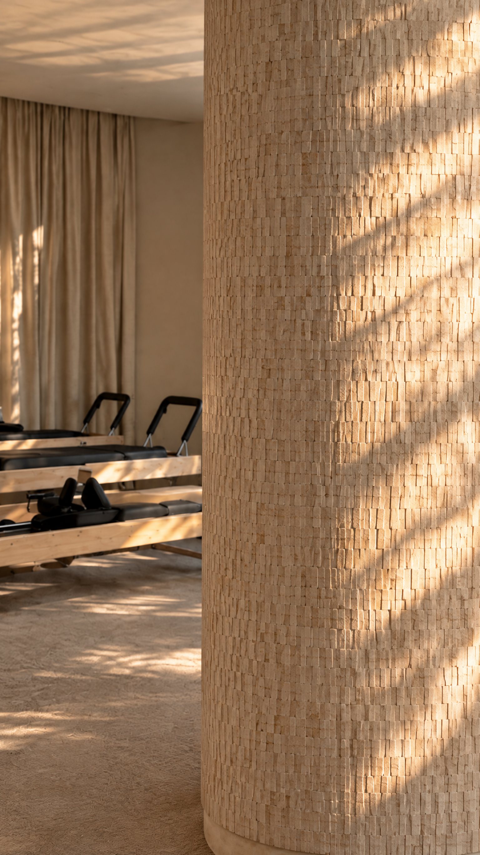 Akasa Studio — Columna de textura mineral bañada por la luz junto a los reformers