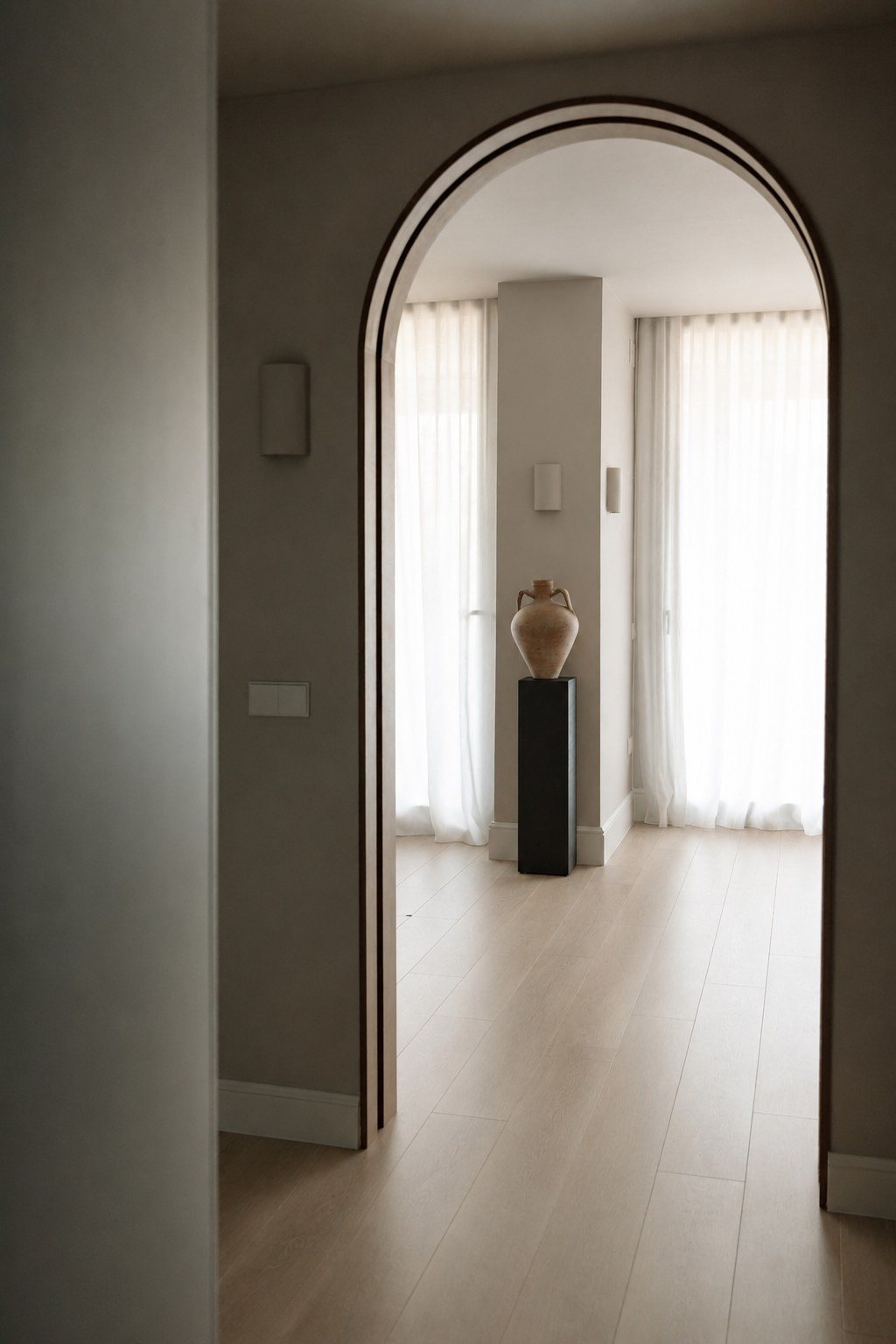 Arco de madera oscura que enmarca un pedestal negro con una pieza cerámica